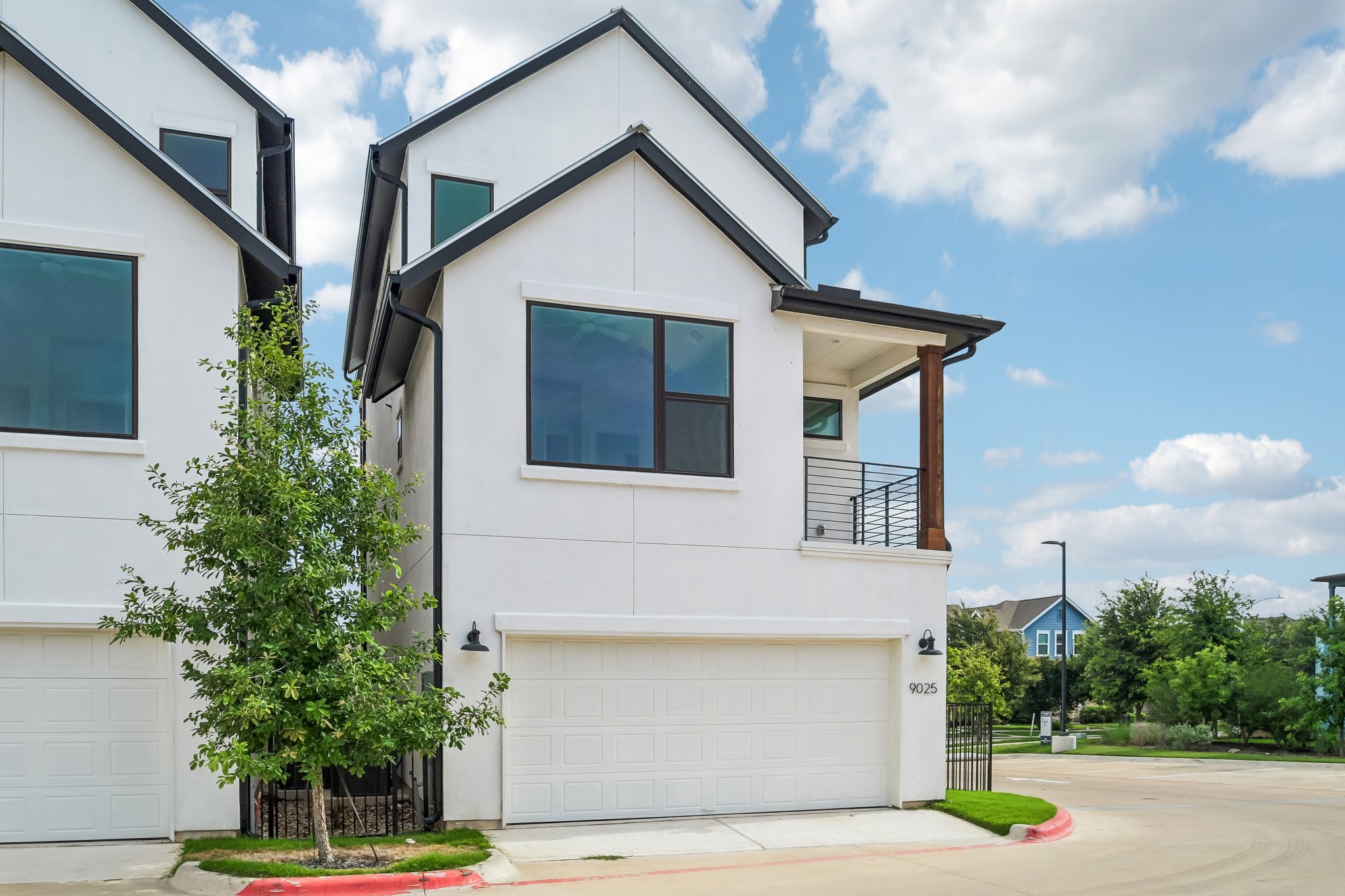 9025 Cattle Baron Path Austin, TX 78747 - Photo 31 of 32 Modern townhome facade showcases clean lines, a ground-level garage, and an elevated balcony with a wood accent column.