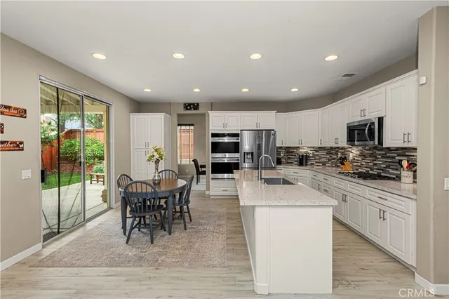 a kitchen with stainless steel appliances kitchen island granite countertop a stove top oven a sink a dining table and chairs with wooden floor
