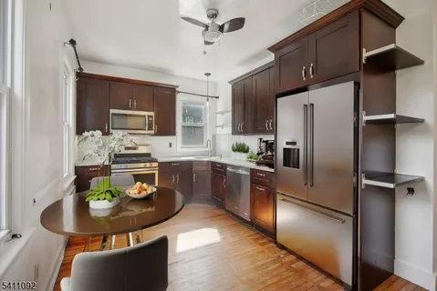 a kitchen with stainless steel appliances granite countertop a refrigerator a stove a sink a dining table and chairs with wooden floor