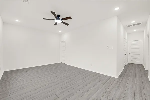 an empty room with wooden floor fan and windows