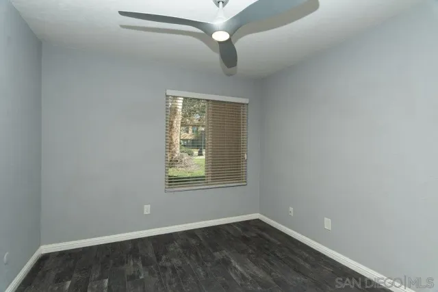 an empty room with wooden floor fan and windows