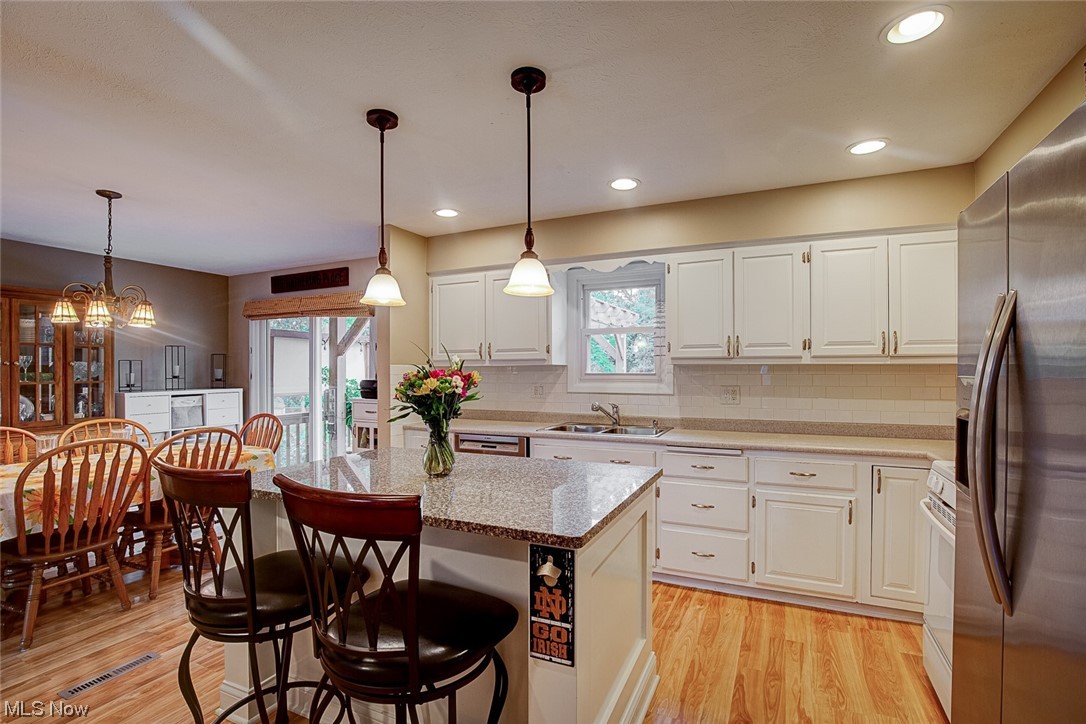 31950 Cannon Road Solon, OH 44139 - Photo 11 of 33 Kitchen featuring decorative light fixtures, backsplash, white cabinetry, a center island with sink, a center island, light hardwood flooring, and stainless steel appliances