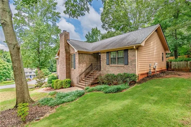 a view of a house with a yard plants and large tree