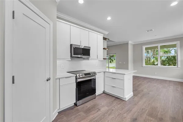 a large kitchen with stainless steel appliances a sink dishwasher a refrigerator and white cabinets with wooden floor