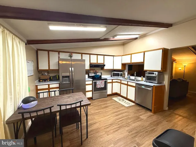 a kitchen with stainless steel appliances kitchen island granite countertop a stove a refrigerator a sink a dining table and chairs with wooden floor