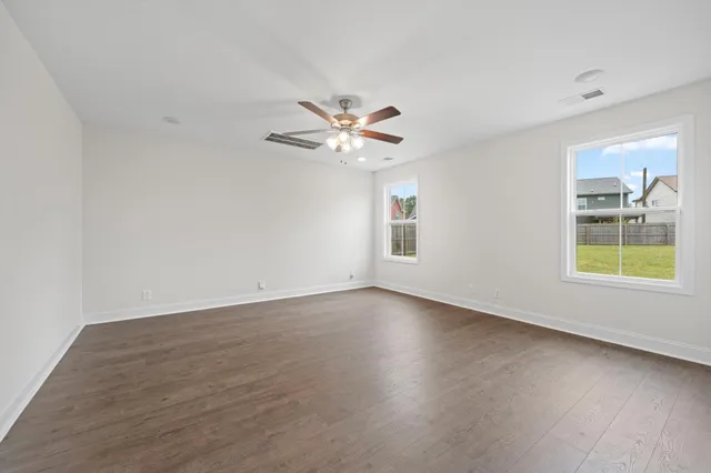 an empty room with wooden floor chandelier fan and windows