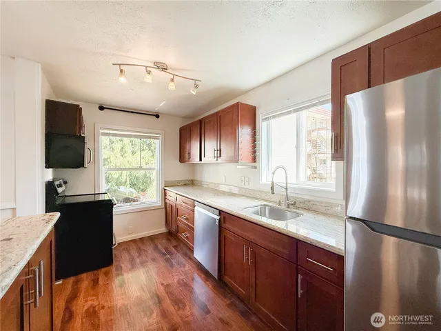 a kitchen with a refrigerator a sink dishwasher a dining table and chairs with wooden floor