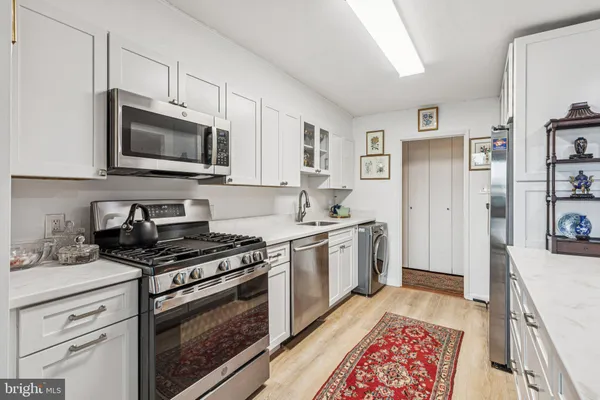 a kitchen with stainless steel appliances granite countertop a stove top oven a sink a refrigerator white cabinets and wooden floor