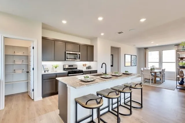 a kitchen with stainless steel appliances granite countertop a stove a refrigerator a kitchen island with a dining table and chairs