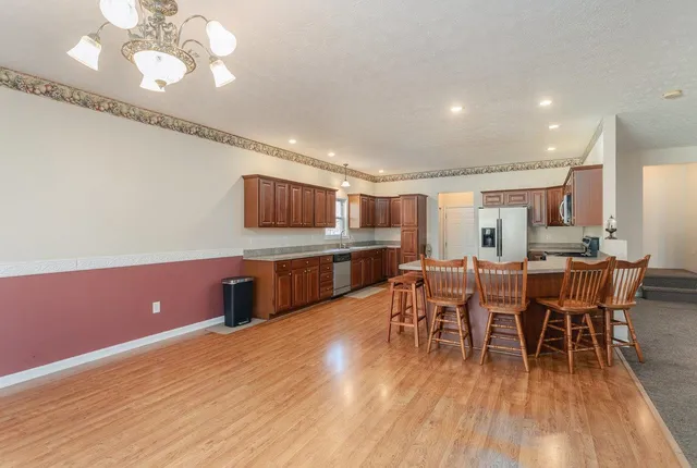 a kitchen with stainless steel appliances kitchen island granite countertop a table chairs and a refrigerator