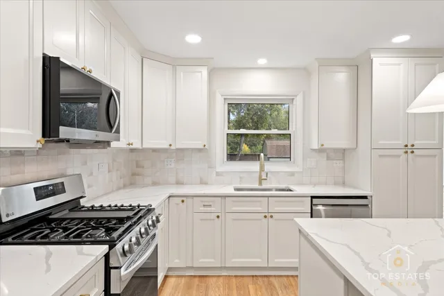 a kitchen with stainless steel appliances kitchen island granite countertop a refrigerator a sink a stove and white cabinets with wooden floor