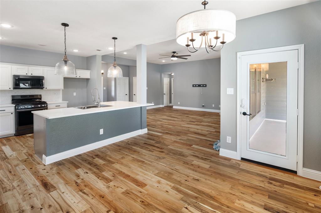 1019 Vaughan Lane Tioga, TX 76271 - Photo 20 of 40 Open-concept living area featuring wood-finish flooring, a kitchen island with a sink and pendant lighting, white cabinetry, and a black range with an overhead microwave