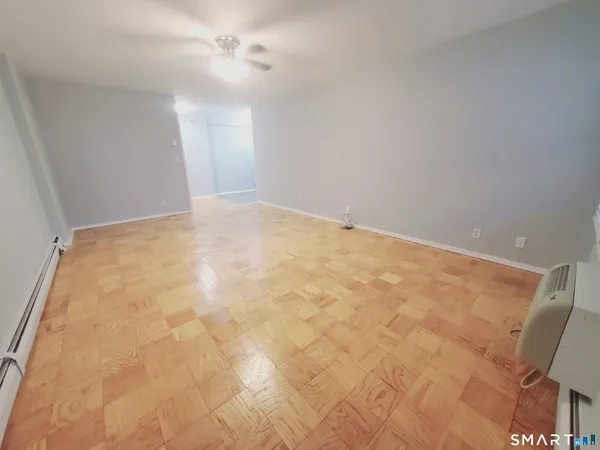 an empty room with a chandelier fan and kitchen view