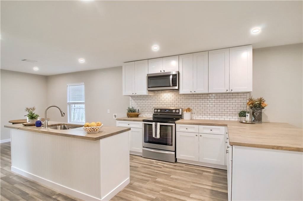 108 Irene Street Elgin, TX 78621 - Photo 1 of 29 Open-concept kitchen featuring an island with an undermount sink, white cabinetry, wood-finish countertops, stainless steel appliances, and subway tile backsplash