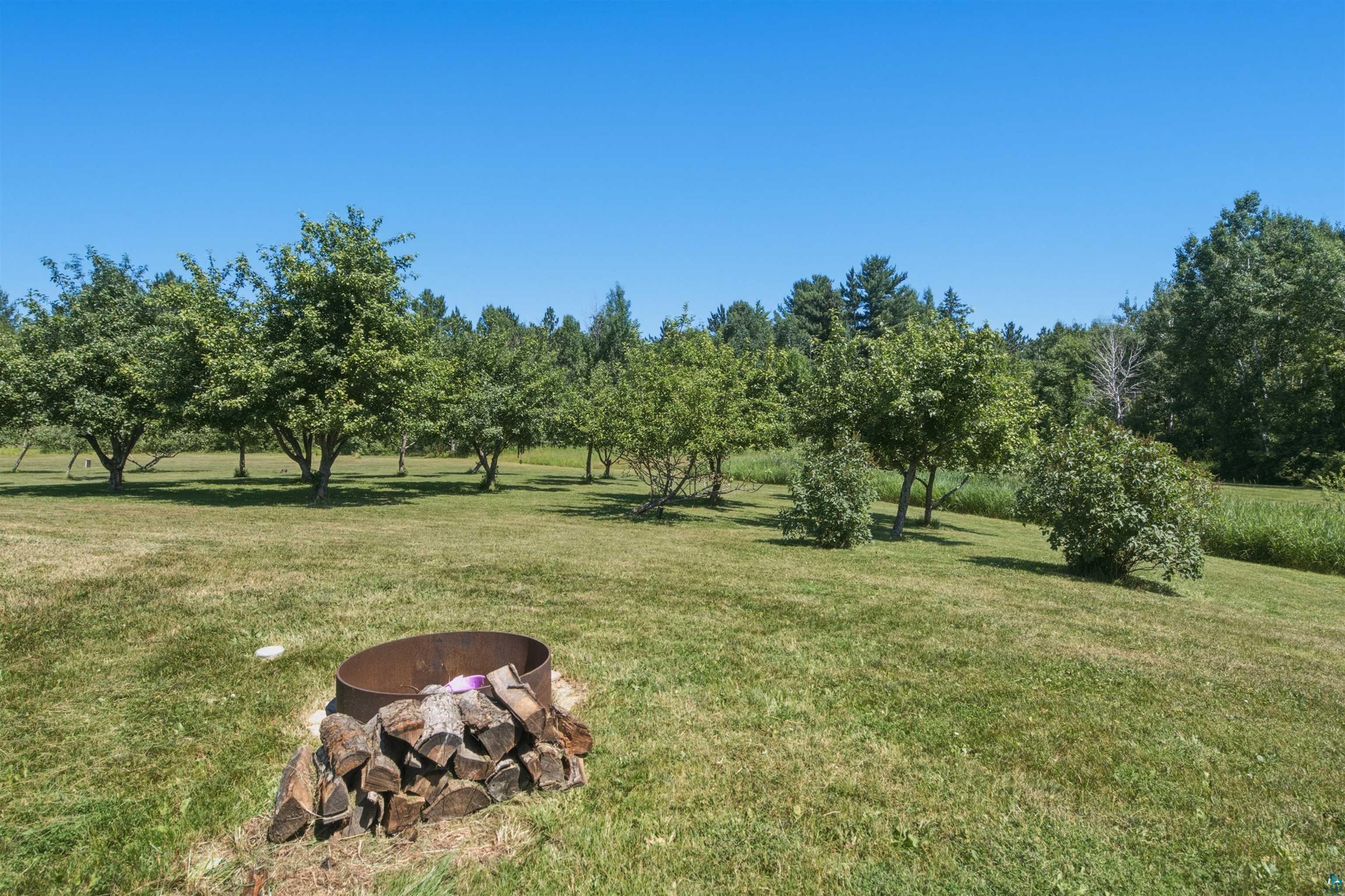 64260 Jolma Road Ashland, WI 54806 - Photo 29 of 35 Expansive lawn area featuring mature trees and a dedicated fire pit with stacked firewood
