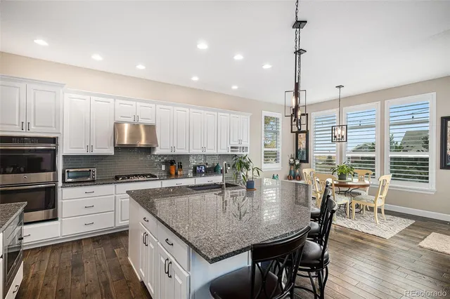 a kitchen with stainless steel appliances granite countertop a stove top oven a sink a dining table and chairs with wooden floor