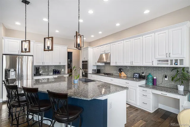 a kitchen with stainless steel appliances granite countertop a sink a stove a refrigerator and chairs