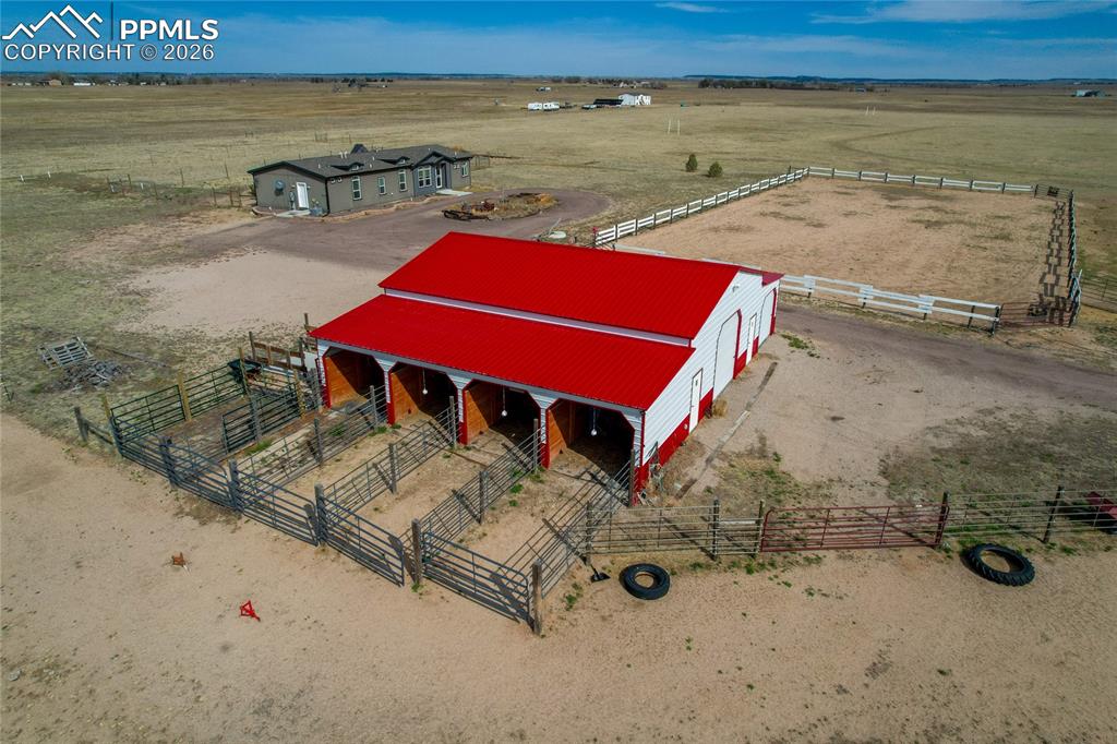 7880 J D Johnson Road Peyton, CO 80831 - Photo 36 of 50 Expansive agricultural property featuring a red and white barn with multiple stalls, a fenced outdoor arena, and additional fenced enclosures