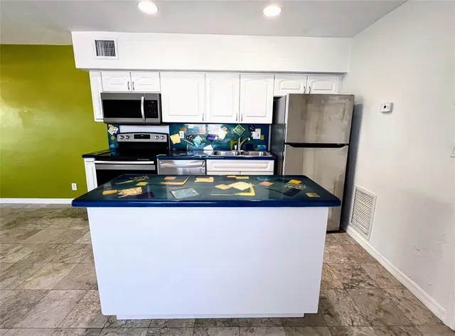 a living room with stainless steel appliances a fireplace a flat screen tv and a window