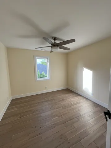 an empty room with wooden floor a ceiling fan and windows