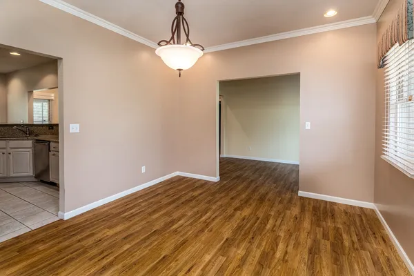 an empty room with wooden floor chandelier and windows