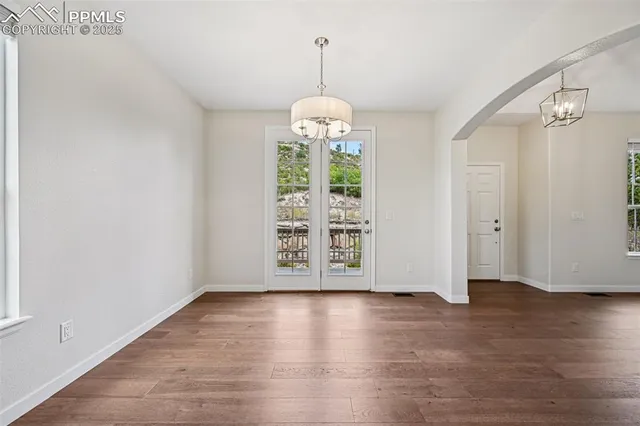 an empty room with wooden floor chandelier and windows