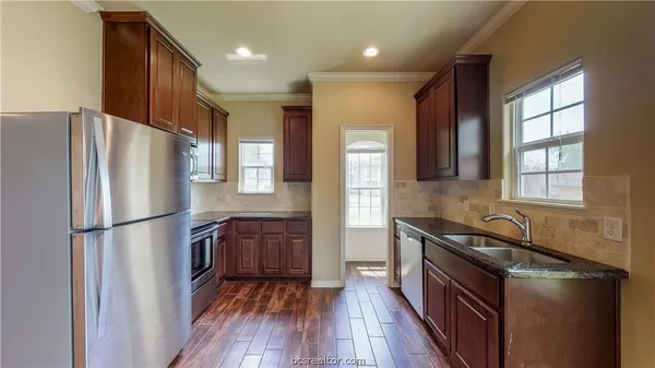 a kitchen with granite countertop stainless steel appliances a refrigerator a sink and wooden cabinets