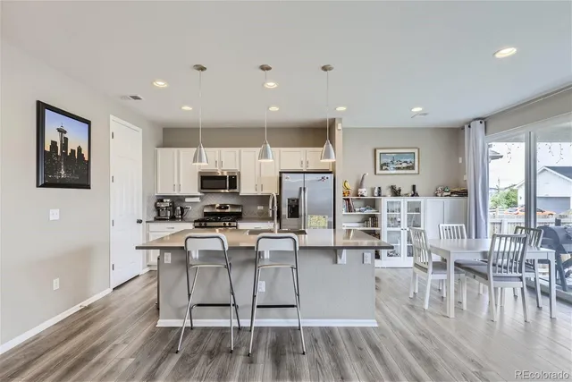a kitchen with stainless steel appliances kitchen island granite countertop a refrigerator a stove top oven and a dining table with wooden floor
