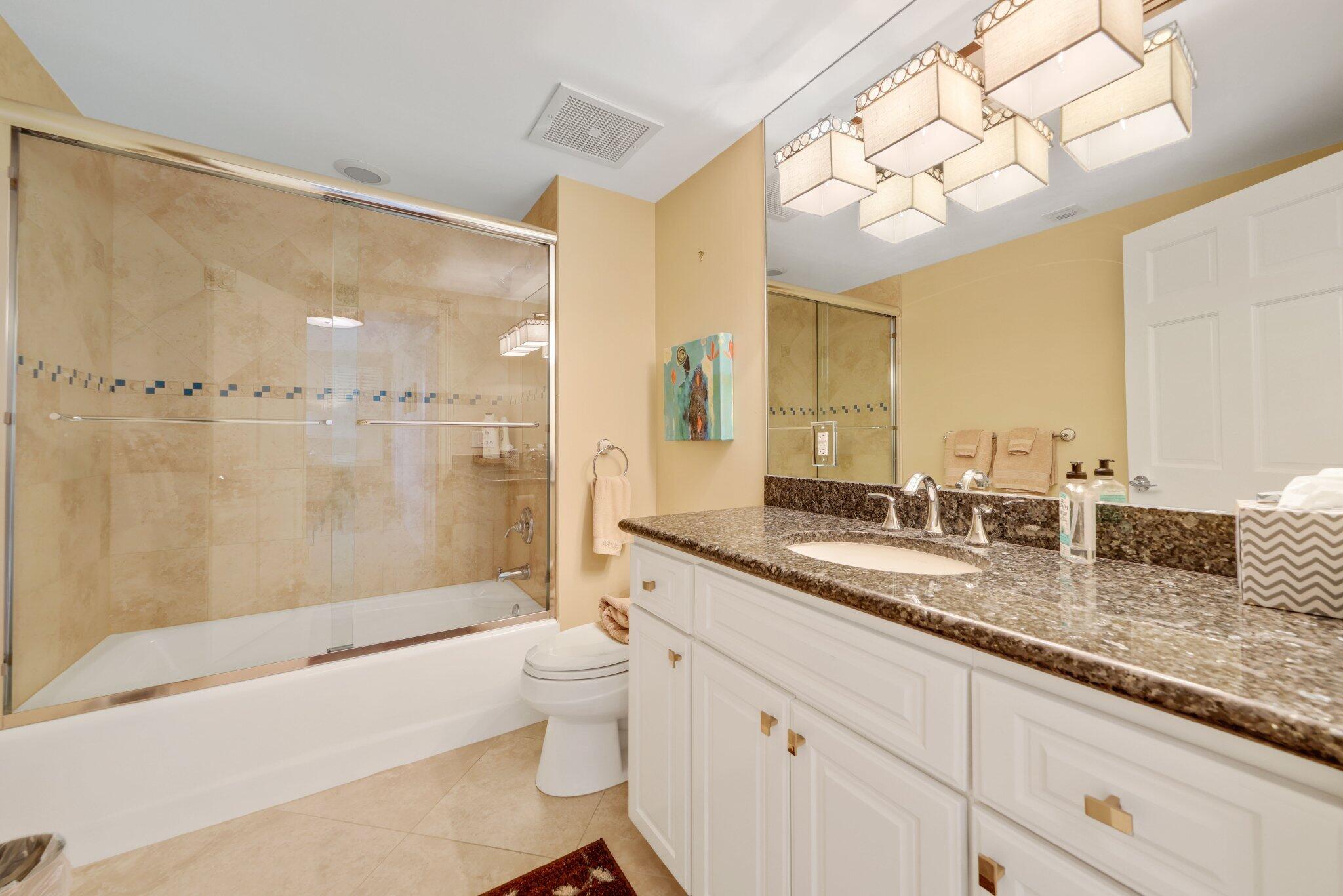 100 Mac Farlane Drive, Unit 3D Delray Beach, FL 33483 - Photo 35 of 57 a bathroom with a granite countertop sink a toilet a large mirror a bathtub and shower