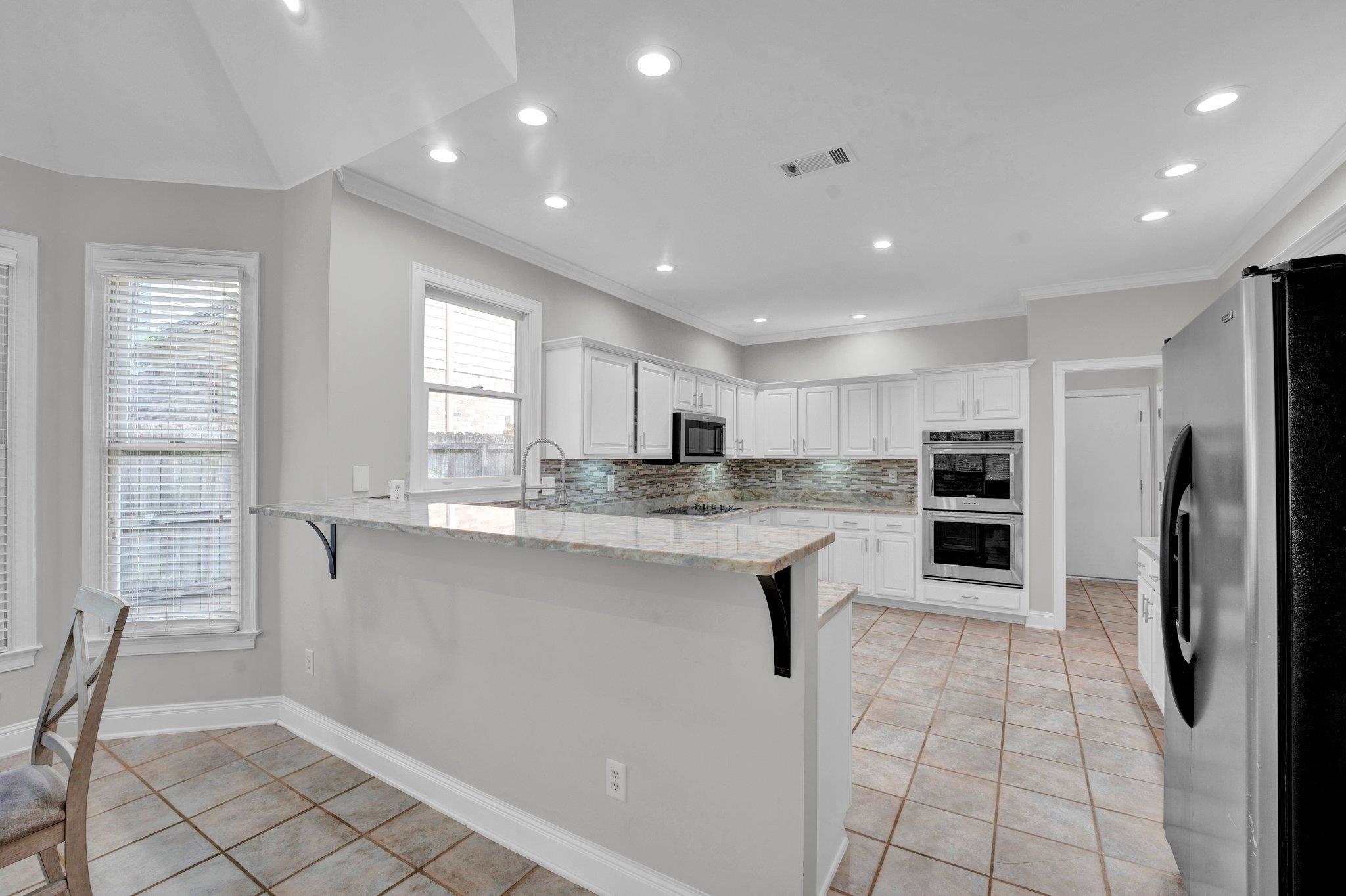 1331 Riding Brook Drive Collierville, TN 38017 - Photo 17 of 39 Kitchen featuring white cabinetry, stainless steel appliances, decorative backsplash, light stone counters, and light tile patterned floors