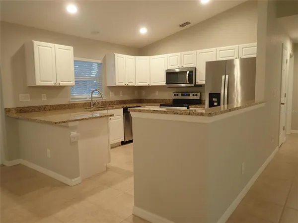 a kitchen with stainless steel appliances granite countertop a sink a stove top oven a refrigerator with white cabinets and a refrigerator