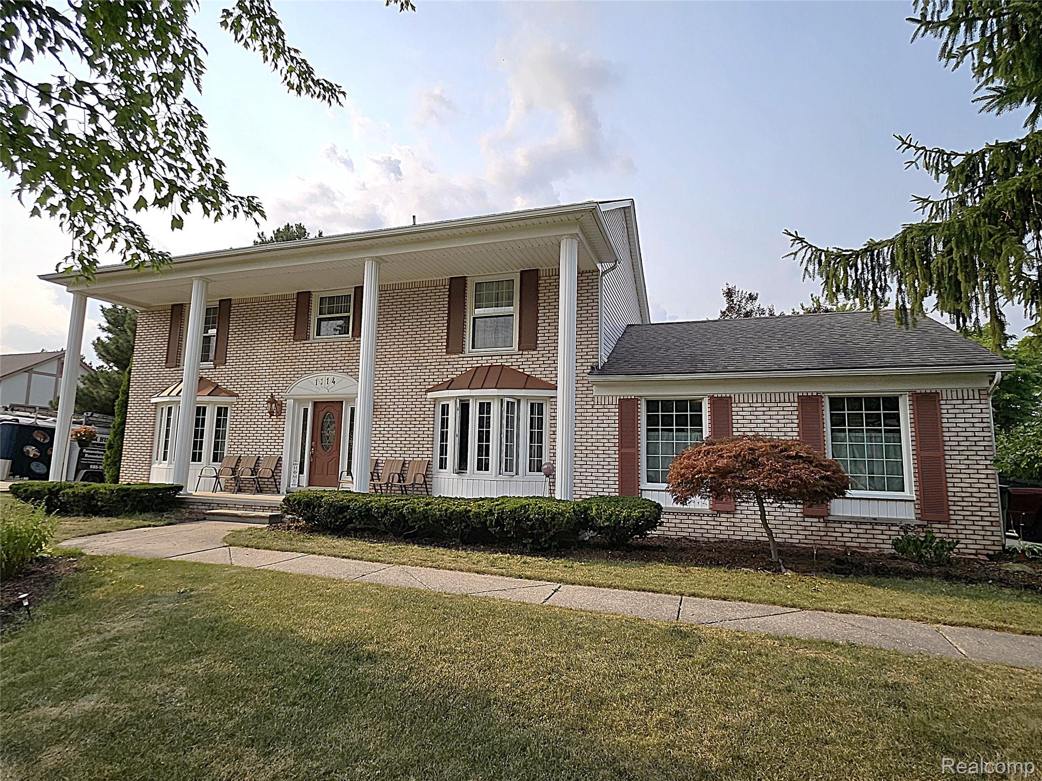 1114 Chaffer Drive Rochester, MI 48306 - Photo 3 of 50 Brick Colonial home featuring a two-story facade with white columns and covered front portico, complemented by a single-story wing with multi-pane windows