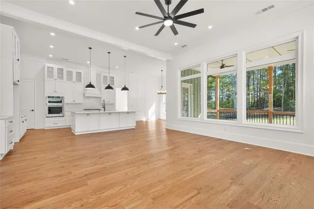 a large white kitchen with kitchen island a refrigerator a stove a sink and a dining table with wooden floor