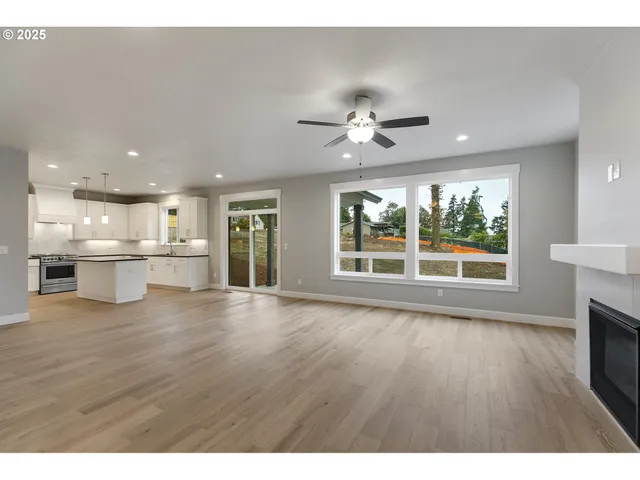 a view of an empty room with wooden floor and a kitchen
