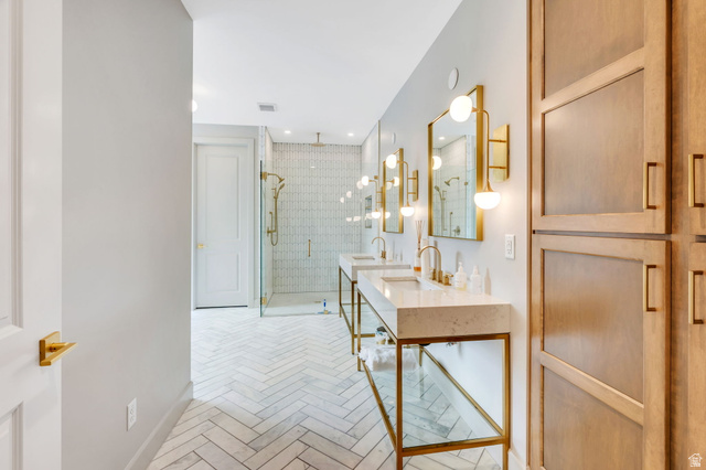 250 South Main Street, Unit 10 Alpine, UT 84004 - Photo 14 of 29 Dual vanity bathroom featuring herringbone tile flooring, a glass-enclosed shower with brass fixtures, and light wood-finish built-in cabinetry