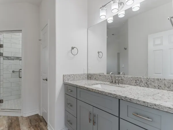 a bathroom with a granite countertop double vanity sink mirror and shower