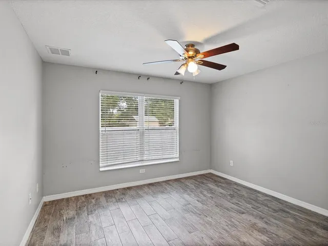 an empty room with wooden floor fan and windows