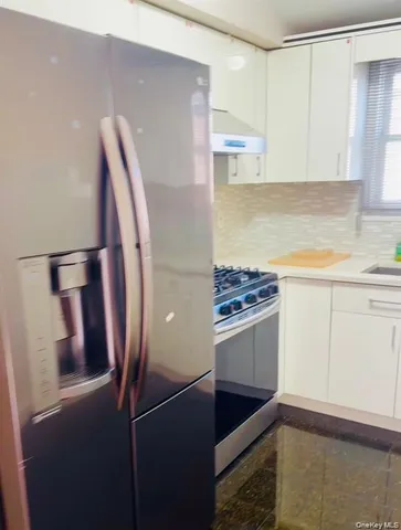 a kitchen with stainless steel appliances granite countertop a refrigerator a stove and white cabinets with wooden floor