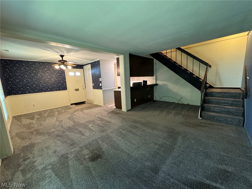 7294 Fox Mill Road, Unit 19D Mentor, OH 44060 - Photo 7 of 27 Carpeted living space featuring a front entry door with transom lites, a ceiling fan with light fixture, wainscoting, and a staircase with metal balusters