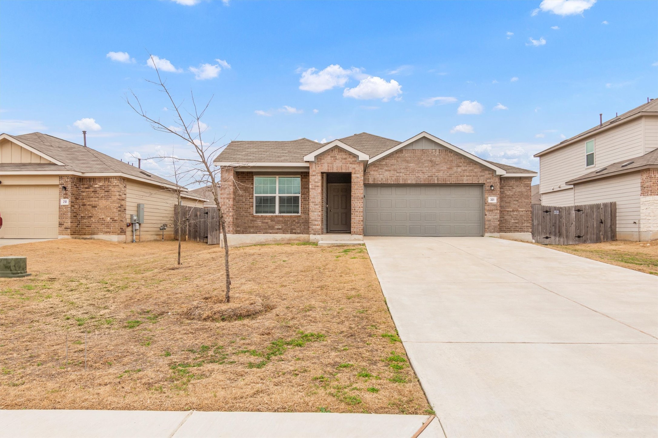 View of front of house with an attached garage, driveway, brick siding, and a gate