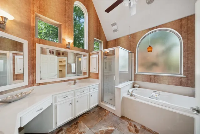 a en suite bathroom with a granite countertop tub a sink and a large mirror next to a window