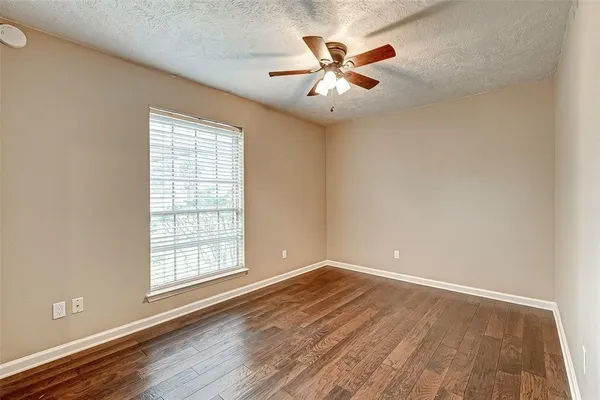 an empty room with wooden floor chandelier fan and windows