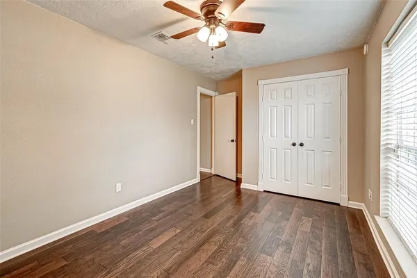 an empty room with wooden floor fan and windows