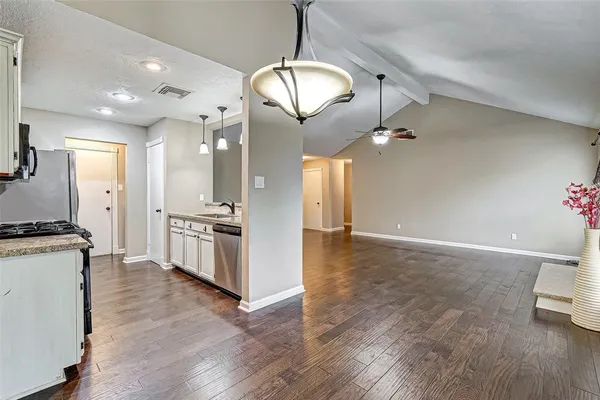 a large kitchen with granite countertop a stove a sink dishwasher a refrigerator and white cabinets with wooden floor