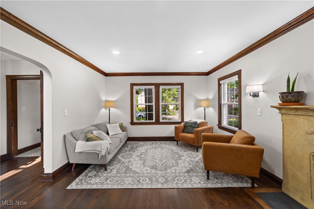 Living room featuring wood finished floors, crown molding, arched walkways, and recessed lighting