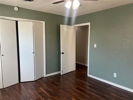 a view of an empty room with wooden floor and a ceiling fan