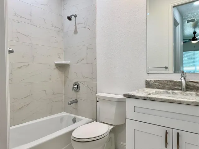 a bathroom with a granite countertop bathtub shower sink vanity and toilet