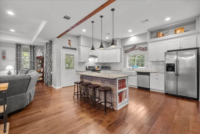 a kitchen with stainless steel appliances kitchen island granite countertop a stove a refrigerator a sink a dining table and chairs with wooden floor