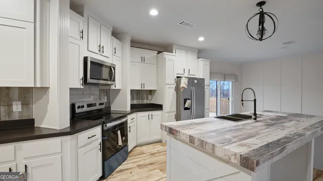 a kitchen with stainless steel appliances kitchen island granite countertop a stove a refrigerator a sink and dishwasher with white cabinets