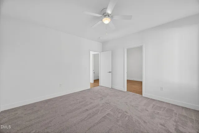 a view of an empty room with wooden floor and a ceiling fan